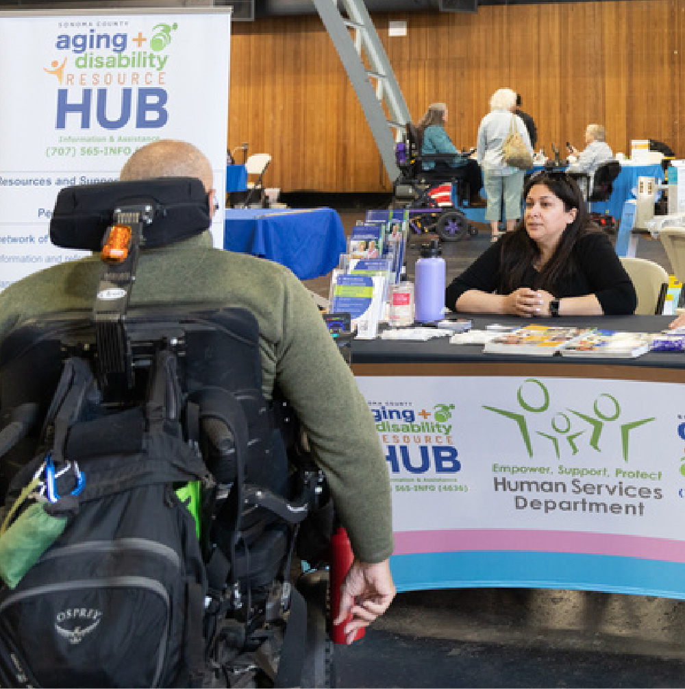 Photo of a man in a power wheelchair talking to a woman at a vendor table.